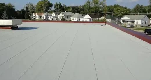 A commercial flat roof with a light grey membrane and a red parapet, houses beyond