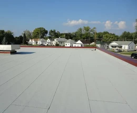 A commercial flat roof with a light grey membrane and a red parapet, houses beyond