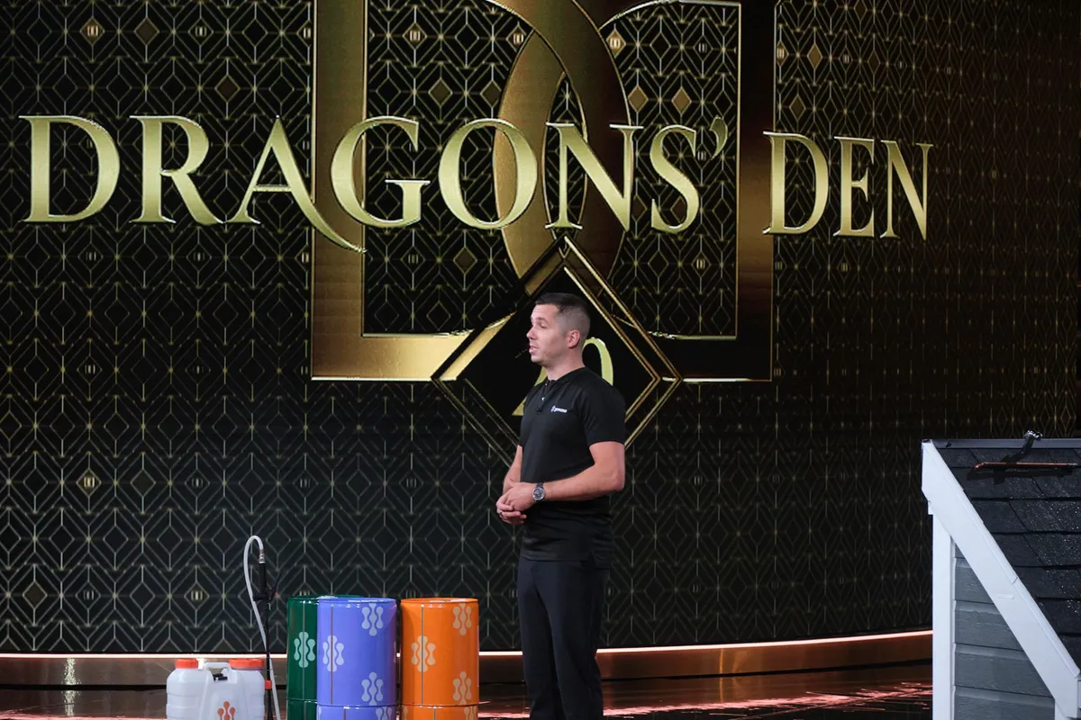 GoNano's founder on the Dragons' Den stage beside three drums of product and a small shingle roof mock-up