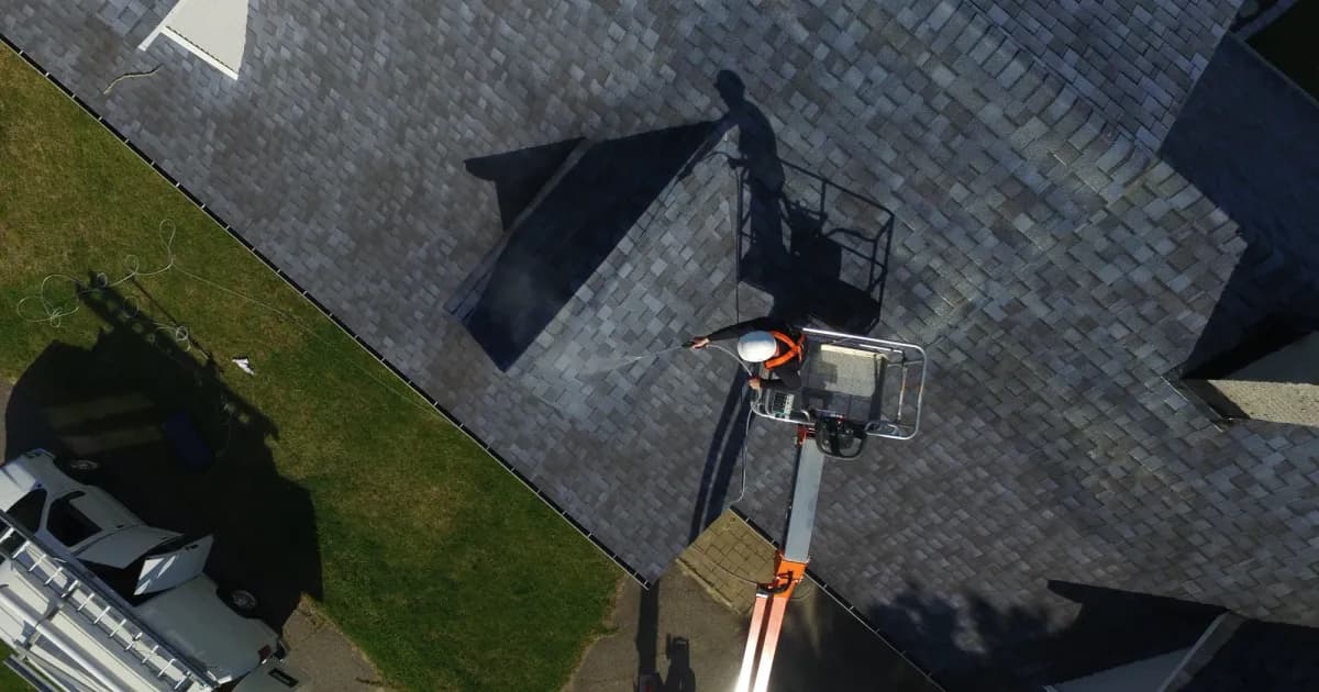Aerial view of an applicator in a boom lift spraying a treatment across an asphalt shingle roof